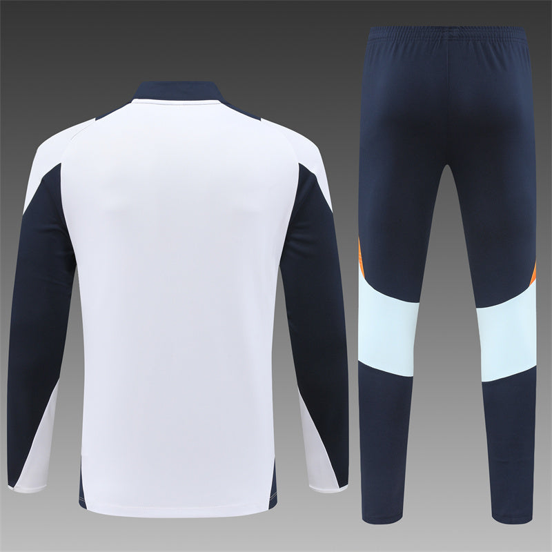 Close-up of the Real Madrid kids' tracksuit, featuring vibrant orange accents on a white base.