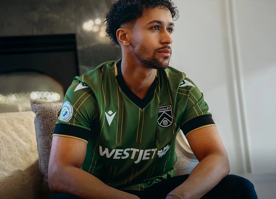 Front view of the Cavalry FC 2025 Macron 50th Anniversary Jersey, featuring green and gold pinstripes.